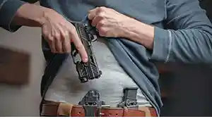 Woman putting handgun back in apendix holster.